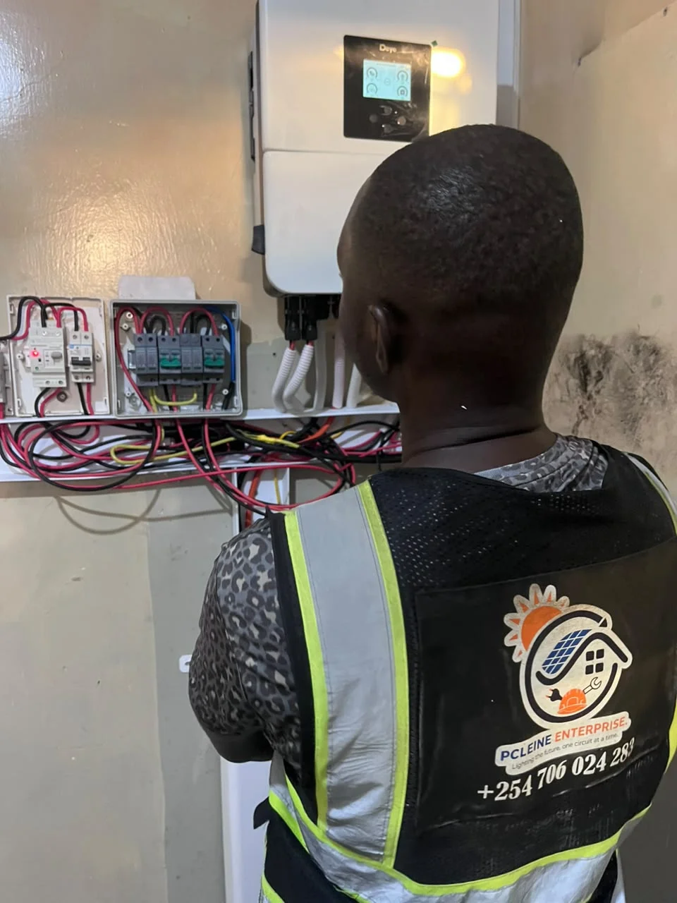 PCLEINE technician in branded company vest inspecting Deye hybrid inverter in Bondeni
